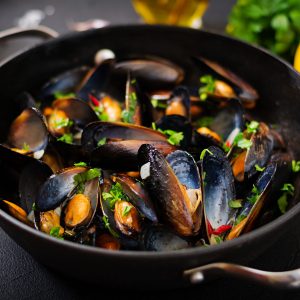 Mussels cooked in wine sauce with herbs in a frying pan on a black background.